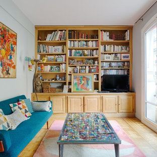 Idée de décoration pour une salle de séjour avec une bibliothèque ou un coin lecture bohème avec un mur gris, un sol en bois clair, un téléviseur encastré et un sol beige.