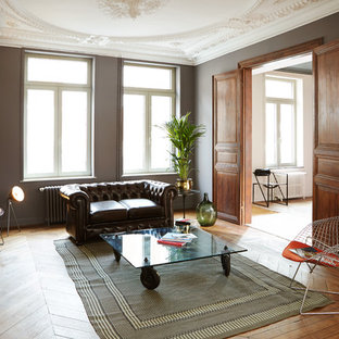 Réalisation d'une grand salle de séjour bohème fermée avec un mur gris, un sol en bois brun, une cheminée standard, un manteau de cheminée en pierre et aucun téléviseur.