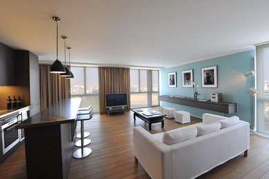 Diseño de sala de estar con barra de bar abierta minimalista grande con paredes azules, suelo de madera clara, televisor independiente y suelo beige