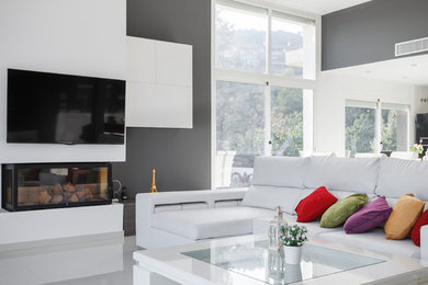 Foto de salón abierto moderno extra grande con paredes grises, chimenea lineal, marco de chimenea de metal, televisor colgado en la pared y suelo blanco