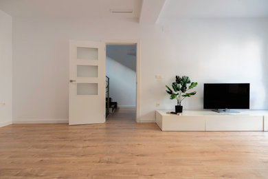 Imagen de salón abierto contemporáneo grande con paredes blancas, suelo de madera clara, televisor independiente y suelo beige