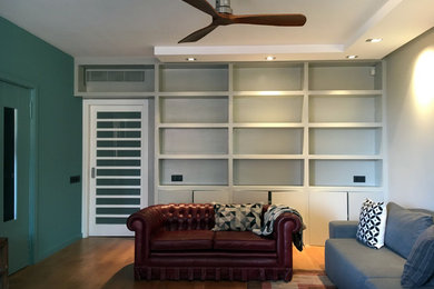 Ejemplo de biblioteca en casa abierta contemporánea con paredes azules, suelo de madera en tonos medios, televisor retractable y suelo beige