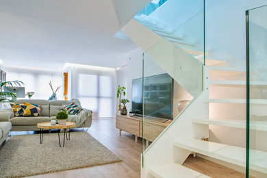Modelo de salón abierto contemporáneo con paredes blancas, suelo de madera clara, televisor independiente y suelo beige