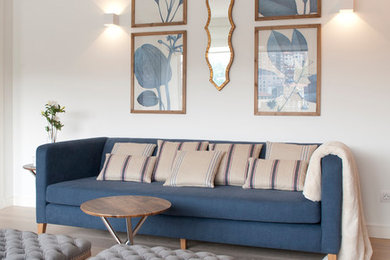 Стильный дизайн: большая открытая гостиная комната в морском стиле с с книжными шкафами и полками, белыми стенами, светлым паркетным полом, бежевым полом и синим диваном - последний тренд