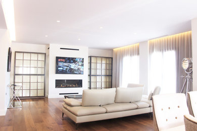 Diseño de salón abierto minimalista grande con paredes blancas, suelo de madera en tonos medios, chimenea lineal, marco de chimenea de metal, televisor colgado en la pared y suelo marrón