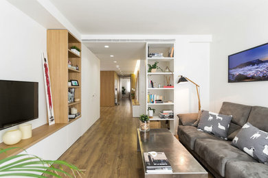 Cette image montre un grand salon design ouvert avec un mur blanc, sol en stratifié, un téléviseur fixé au mur, un sol marron et éclairage.