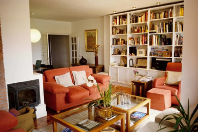 Ejemplo de biblioteca en casa abierta clásica renovada de tamaño medio sin televisor con paredes blancas, suelo de madera en tonos medios, estufa de leña y marco de chimenea de yeso
