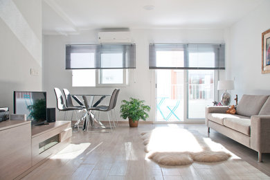 Foto de salón abierto actual de tamaño medio sin chimenea con paredes blancas, suelo de madera clara y televisor independiente