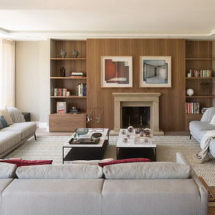 Diseño de biblioteca en casa actual, grande, sin televisor, con paredes beige, chimenea tradicional y suelo de madera en tonos medios