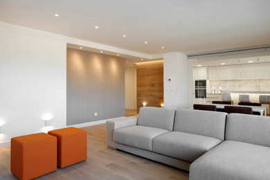 Modelo de salón abierto actual de tamaño medio con paredes beige, suelo laminado y televisor colgado en la pared