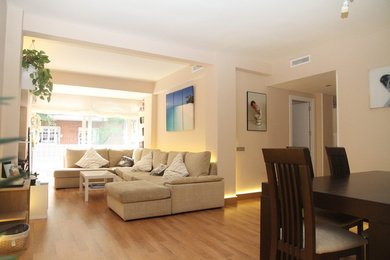 Foto de salón para visitas abierto contemporáneo de tamaño medio sin chimenea con paredes beige, suelo de madera en tonos medios y pared multimedia