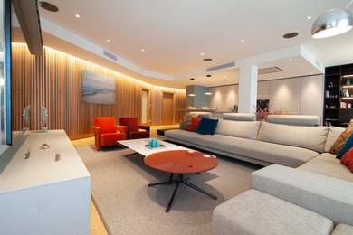 Diseño de salón abierto grande sin chimenea con paredes beige, suelo de madera en tonos medios y televisor colgado en la pared