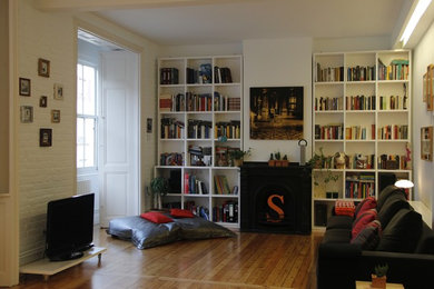 Imagen de biblioteca en casa contemporánea de tamaño medio con paredes blancas, suelo de madera clara, todas las chimeneas, marco de chimenea de metal y televisor independiente