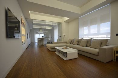 Modelo de salón para visitas abierto actual de tamaño medio sin chimenea con paredes blancas, suelo de madera en tonos medios y televisor colgado en la pared