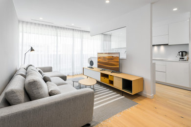Foto de salón abierto contemporáneo con paredes blancas, suelo de madera clara, televisor independiente y suelo beige