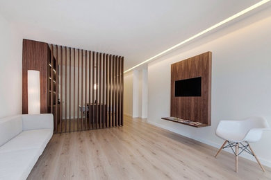 Modelo de salón para visitas abierto contemporáneo grande con paredes blancas, suelo de madera clara y televisor colgado en la pared
