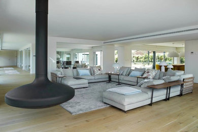 Modelo de salón para visitas abierto contemporáneo extra grande sin televisor con paredes blancas, suelo de madera en tonos medios y chimeneas suspendidas