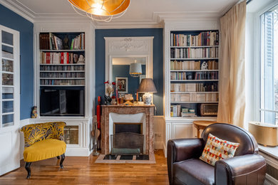 Aménagement d'un salon classique de taille moyenne et fermé avec une bibliothèque ou un coin lecture, un mur bleu, un sol en bois brun, une cheminée standard, un téléviseur fixé au mur et un sol marron.