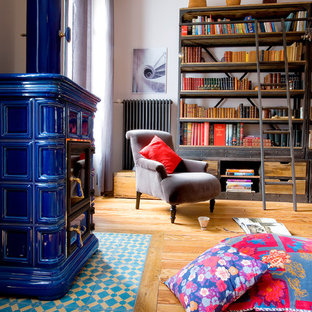 Imagen de biblioteca en casa ecléctica con paredes rosas, suelo de madera en tonos medios, marco de chimenea de baldosas y/o azulejos y estufa de leña