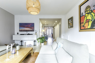 Modern inredning av ett mellanstort vardagsrum, med vita väggar, ljust trägolv och en väggmonterad TV