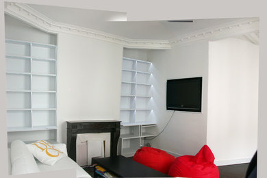 На фото: изолированная гостиная комната среднего размера в современном стиле с с книжными шкафами и полками, белыми стенами, темным паркетным полом, стандартным камином, фасадом камина из камня, мультимедийным центром и коричневым полом