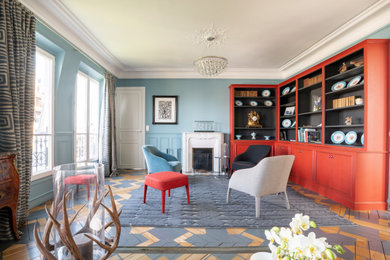 Cette photo montre un grand salon chic avec une bibliothèque ou un coin lecture, un mur bleu, parquet peint, une cheminée standard, un manteau de cheminée en pierre et un sol gris.