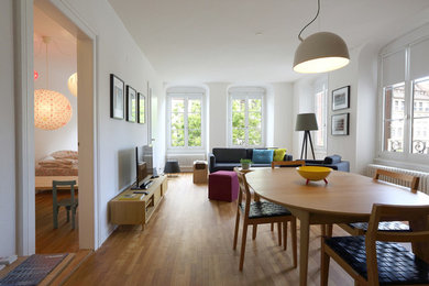 Modelo de salón abierto actual con paredes blancas, suelo de madera en tonos medios y televisor independiente