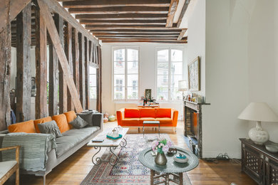 Cette image montre un grand salon design ouvert avec un mur blanc, un manteau de cheminée en brique, un sol marron, parquet clair, une cheminée double-face et poutres apparentes.