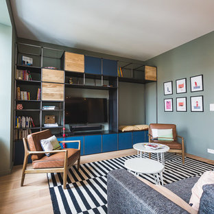 Cette image montre un salon avec une bibliothèque ou un coin lecture design de taille moyenne et fermé avec un mur vert, un sol en bois clair, aucune cheminée et un téléviseur fixé au mur.