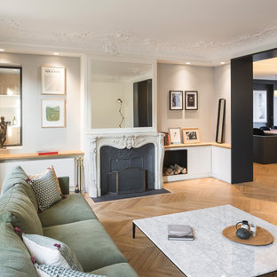 Cette photo montre un grand salon tendance fermé avec un mur gris, un sol en bois clair, une cheminée standard, un téléviseur fixé au mur, un manteau de cheminée en métal et un sol marron.