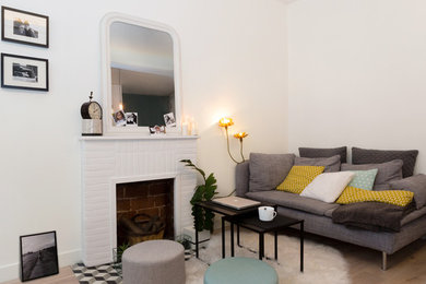 Idée de décoration pour un petit salon design fermé avec un mur blanc, parquet clair, une cheminée standard, un manteau de cheminée en brique, un sol gris et aucun téléviseur.