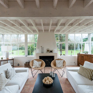 Idées déco pour un salon bord de mer avec un mur blanc, un sol en carreau de terre cuite, une cheminée standard, un manteau de cheminée en pierre et un sol beige.