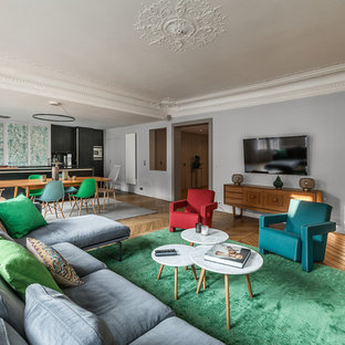Réalisation d'un petit salon design ouvert et haussmannien avec un mur gris, un sol en bois brun, un téléviseur fixé au mur et un sol marron.