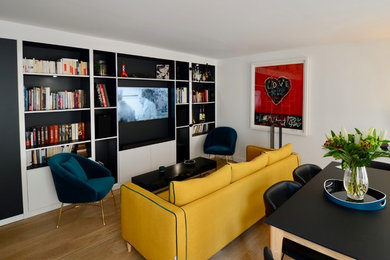 Diseño de biblioteca en casa abierta contemporánea de tamaño medio sin chimenea con paredes blancas, suelo de madera clara y televisor colgado en la pared