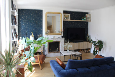 Cette photo montre un salon chic avec une bibliothèque ou un coin lecture, un mur bleu, parquet clair, une cheminée standard, un manteau de cheminée en carrelage, un téléviseur indépendant et du papier peint.