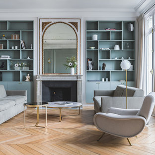 Inspiration pour un salon design ouvert avec un mur gris, un sol en bois clair, une cheminée standard, un manteau de cheminée en brique et un sol beige.