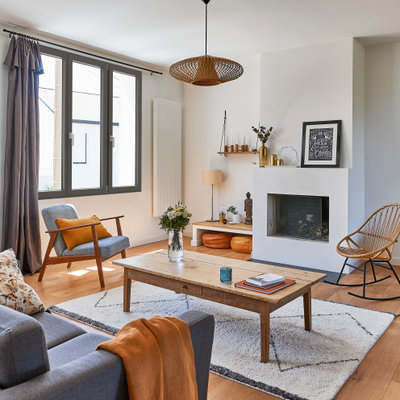 Mid-sized danish medium tone wood floor and beige floor living room photo in Paris with white walls, a standard fireplace and a plaster fireplace