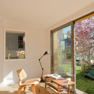 Cette image montre un salon avec une bibliothèque ou un coin lecture nordique ouvert et de taille moyenne avec un mur blanc, un sol en bois clair, aucune cheminée et aucun téléviseur.