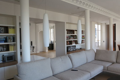 Modelo de salón abierto actual grande con paredes blancas, suelo de madera clara y suelo beige
