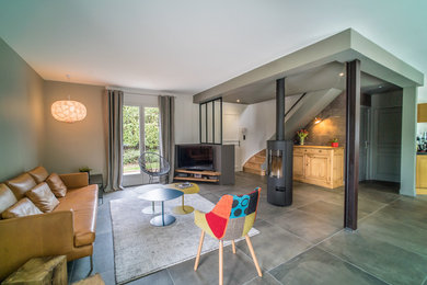 Cette photo montre un salon tendance avec un mur beige, un sol en carrelage de céramique, un poêle à bois, un manteau de cheminée en métal et un sol gris.
