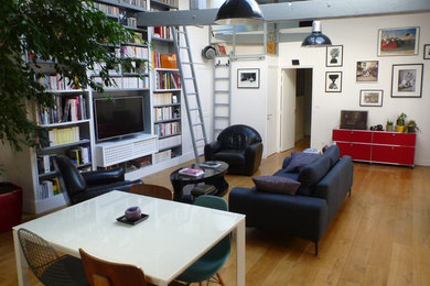 Exemple d'un grand salon industriel ouvert avec une bibliothèque ou un coin lecture, un mur blanc, parquet clair, aucune cheminée, un téléviseur indépendant et un sol marron.