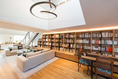 Cette photo montre un grand salon chic ouvert avec une bibliothèque ou un coin lecture, un mur blanc, parquet clair, aucune cheminée, aucun téléviseur et un sol beige.