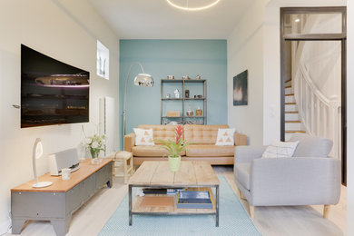 Cette image montre un salon urbain de taille moyenne et ouvert avec un mur bleu, parquet clair, une cheminée d'angle, un manteau de cheminée en plâtre, un téléviseur fixé au mur et un sol beige.