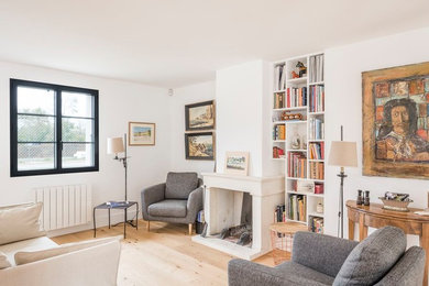 Exemple d'un salon tendance avec une bibliothèque ou un coin lecture, un mur blanc, un sol en bois brun, une cheminée standard, un sol marron et éclairage.