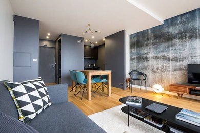 Modelo de salón para visitas abierto actual grande sin chimenea con paredes grises, suelo de madera clara, televisor colgado en la pared y suelo gris