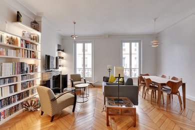 Mittelgroße, Offene Moderne Bibliothek mit grauer Wandfarbe, hellem Holzboden, Kamin, Kaminumrandung aus Holz und freistehendem TV in Paris