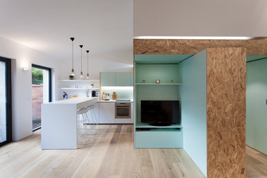 Cette photo montre un petit salon scandinave ouvert avec un mur vert, un sol en bois brun et un téléviseur dissimulé.