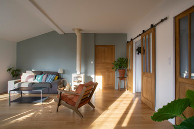 Modelo de salón abierto retro de tamaño medio sin televisor con paredes grises, suelo de madera clara y estufa de leña