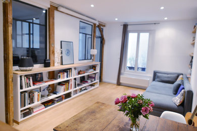 Cette image montre un salon urbain de taille moyenne et ouvert avec une bibliothèque ou un coin lecture, un mur blanc, parquet clair et un téléviseur dissimulé.