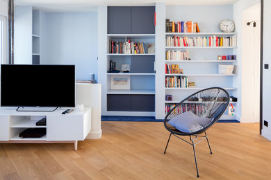 Cette photo montre un salon blanc et bois tendance de taille moyenne et ouvert avec une bibliothèque ou un coin lecture, un mur bleu, parquet clair, aucune cheminée, un téléviseur indépendant et un sol beige.
